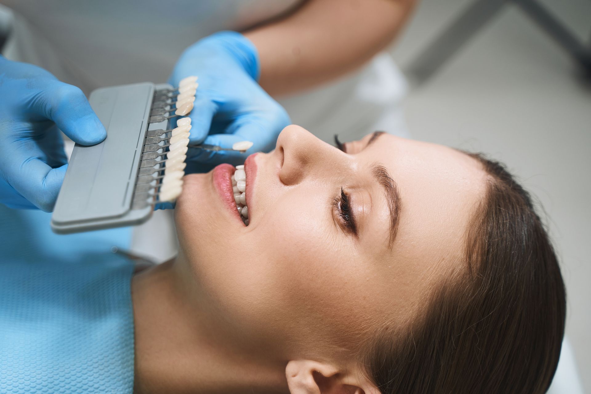 The dentist is helping a patient in the chair with choosing a color before getting veneers.