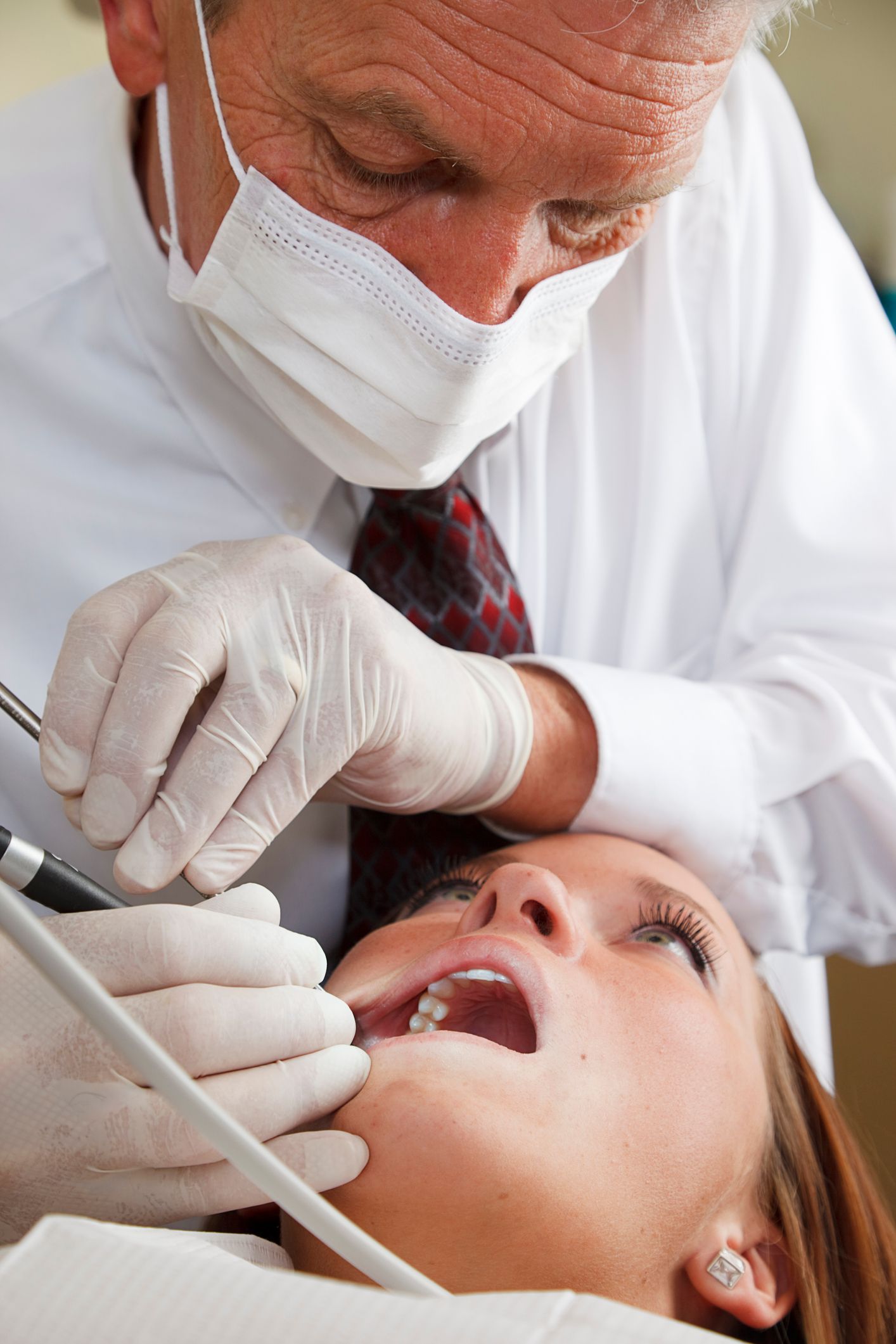 Dentist in mask and gloves examining a patient’s open mouth with dental tools in a clinic.