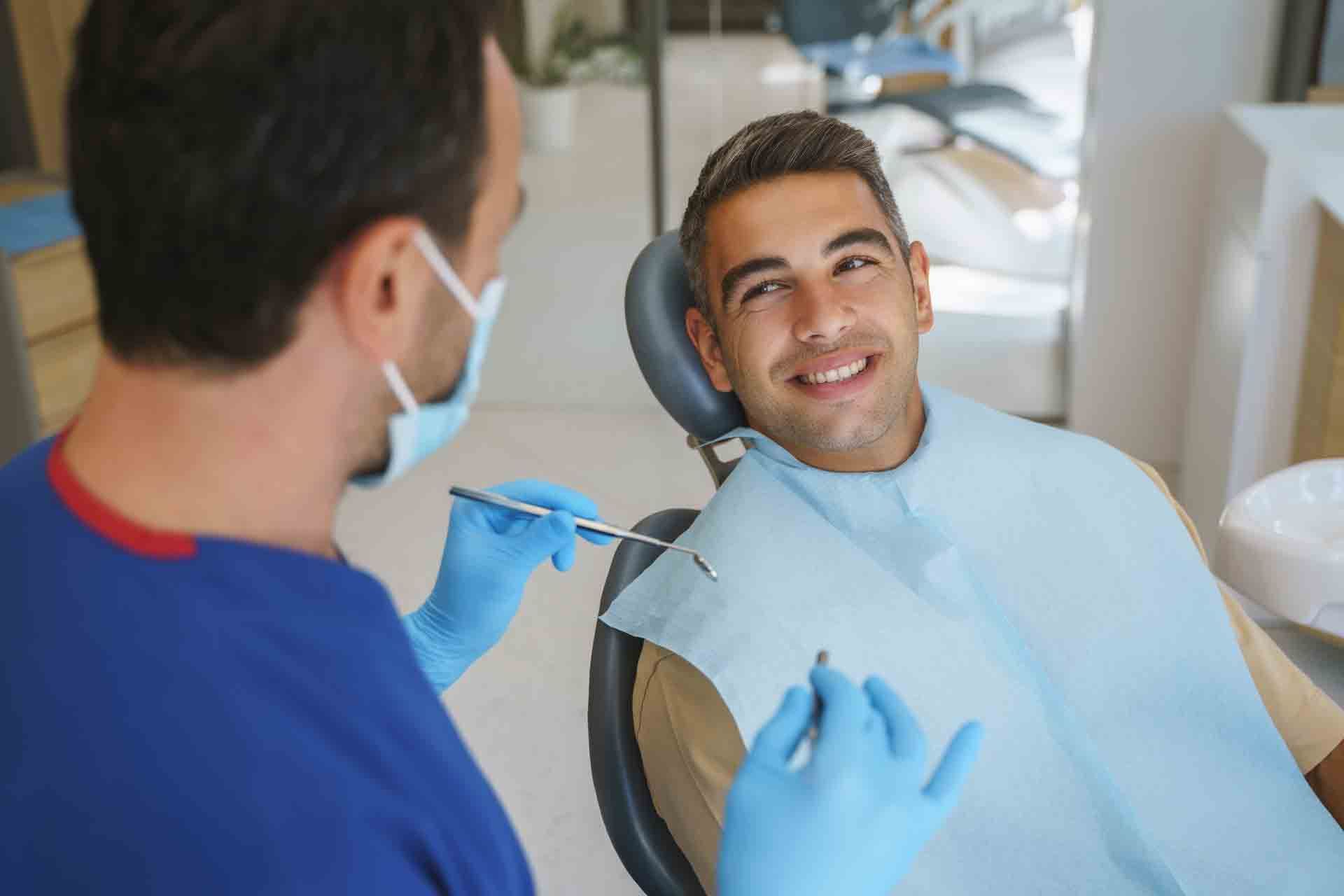 A man is sitting in a dental chair while a dentist examines his teeth. Jackson Heights, NY — Vanguard and Achury Dental