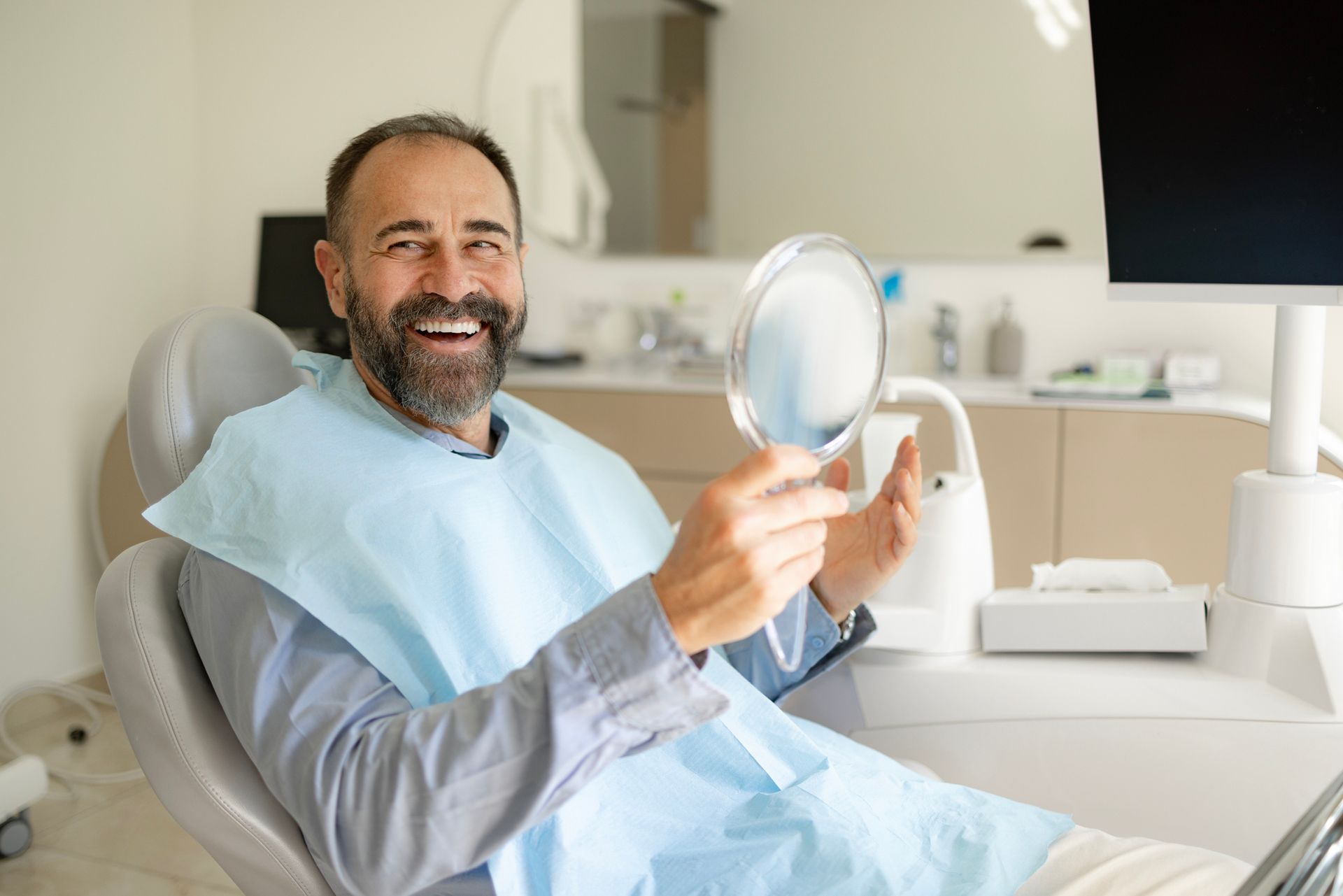 A man is sitting in a dental chair holding a magnifying glass. Jackson Heights, NY — Vanguard and Achury Dental