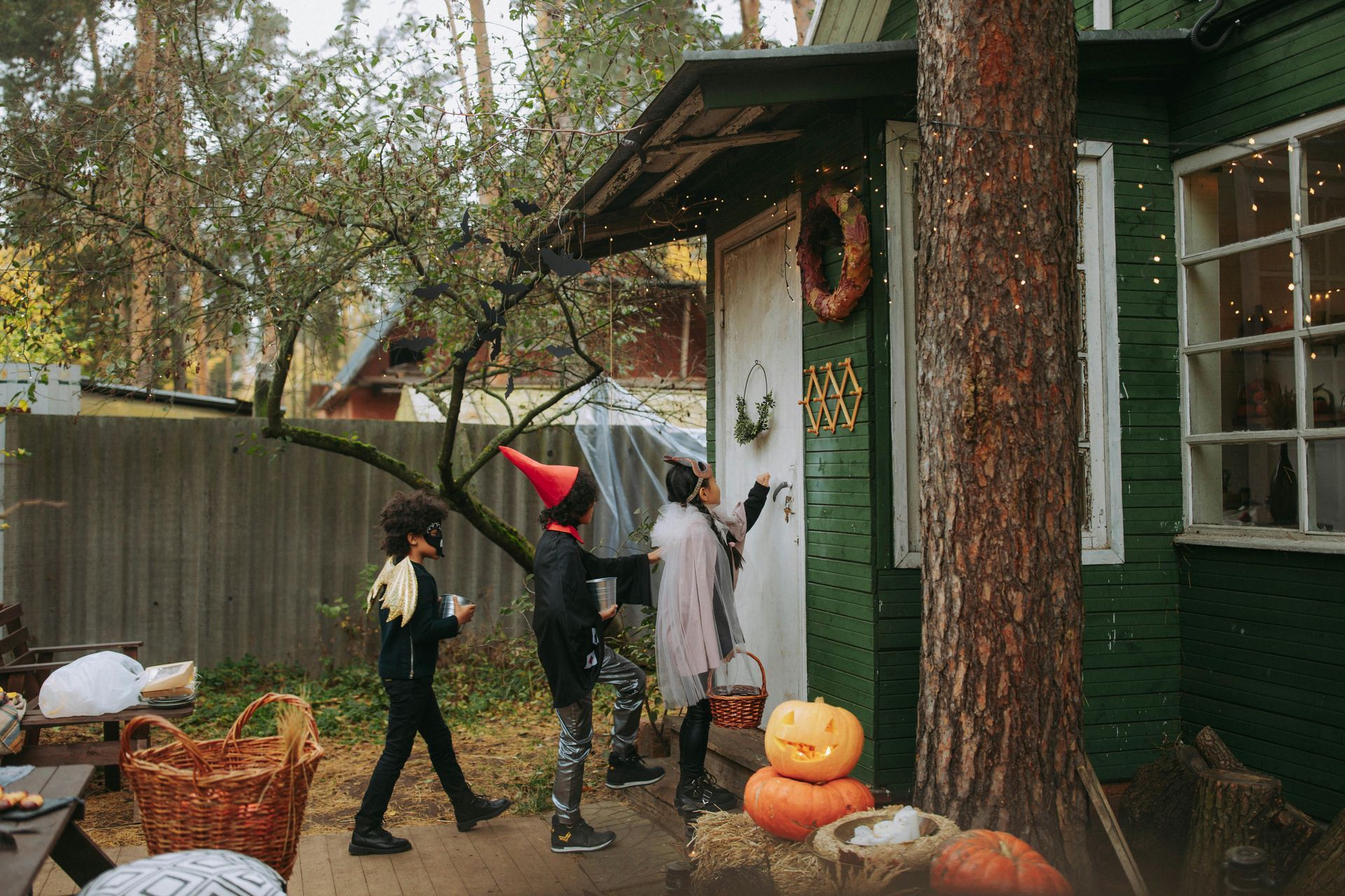 A group of children in halloween costumes are trick or treating in front of a green house.