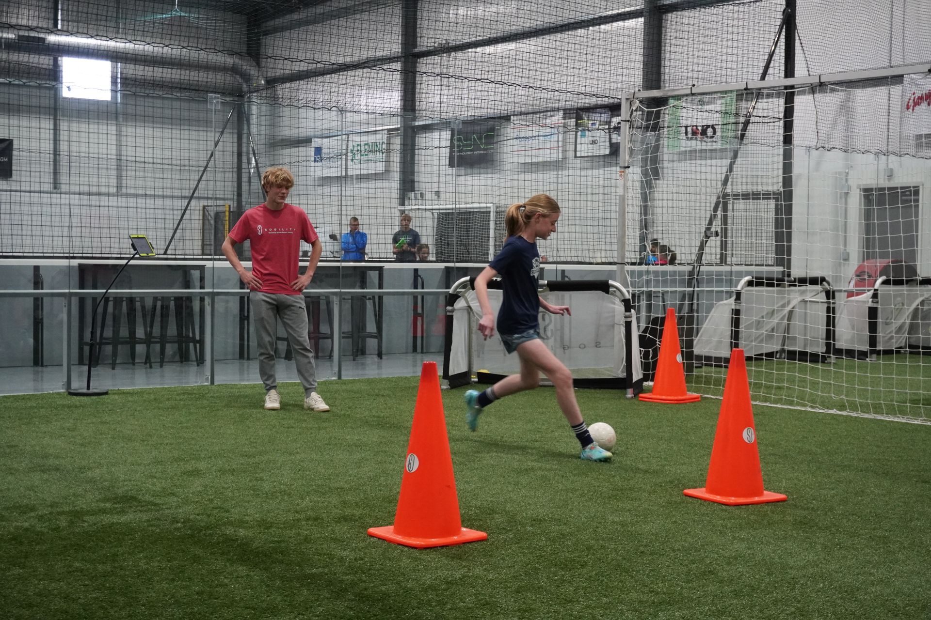 A girl is kicking a soccer ball between two orange cones on a field.