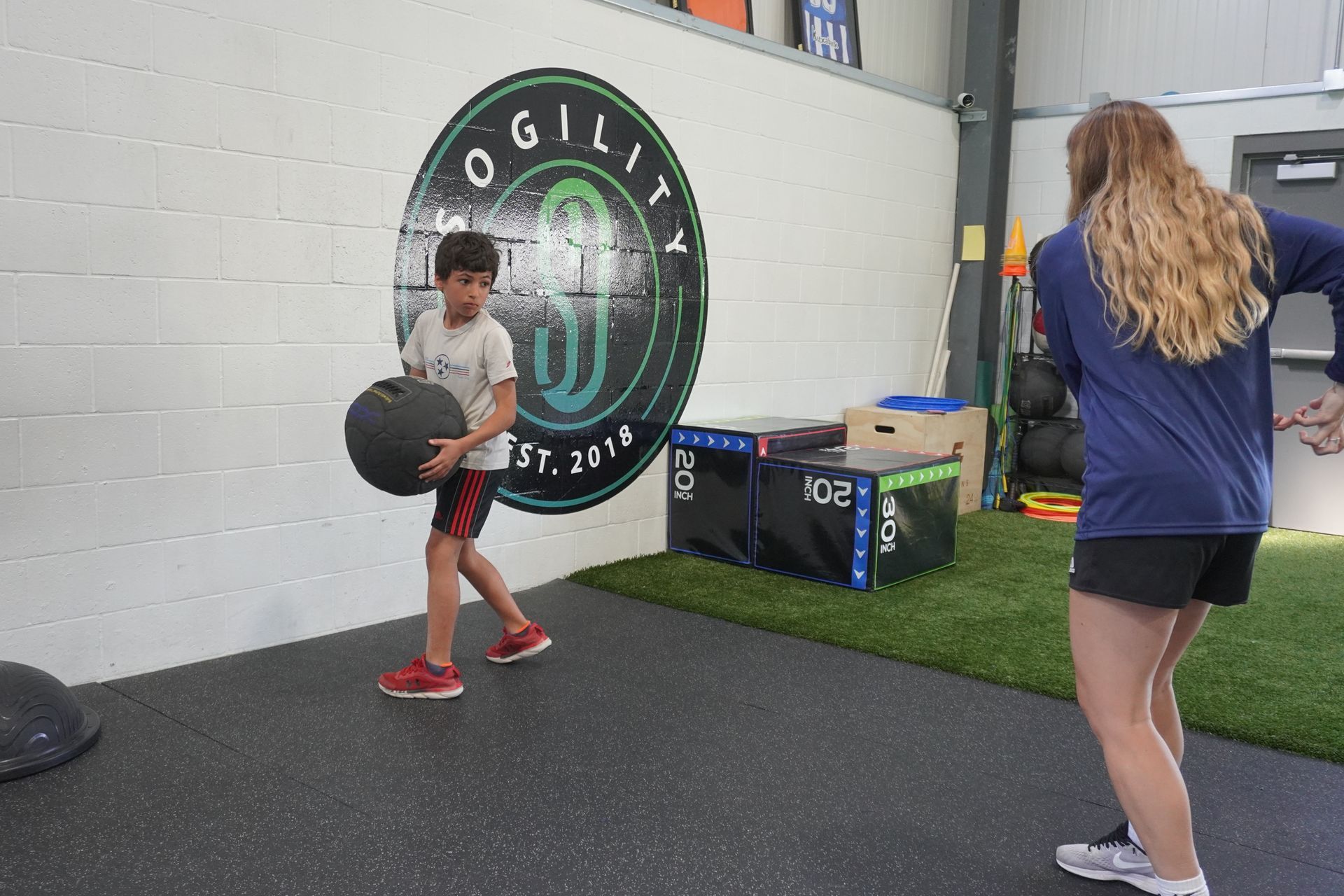 A girl is standing next to a boy holding a medicine ball in a gym.