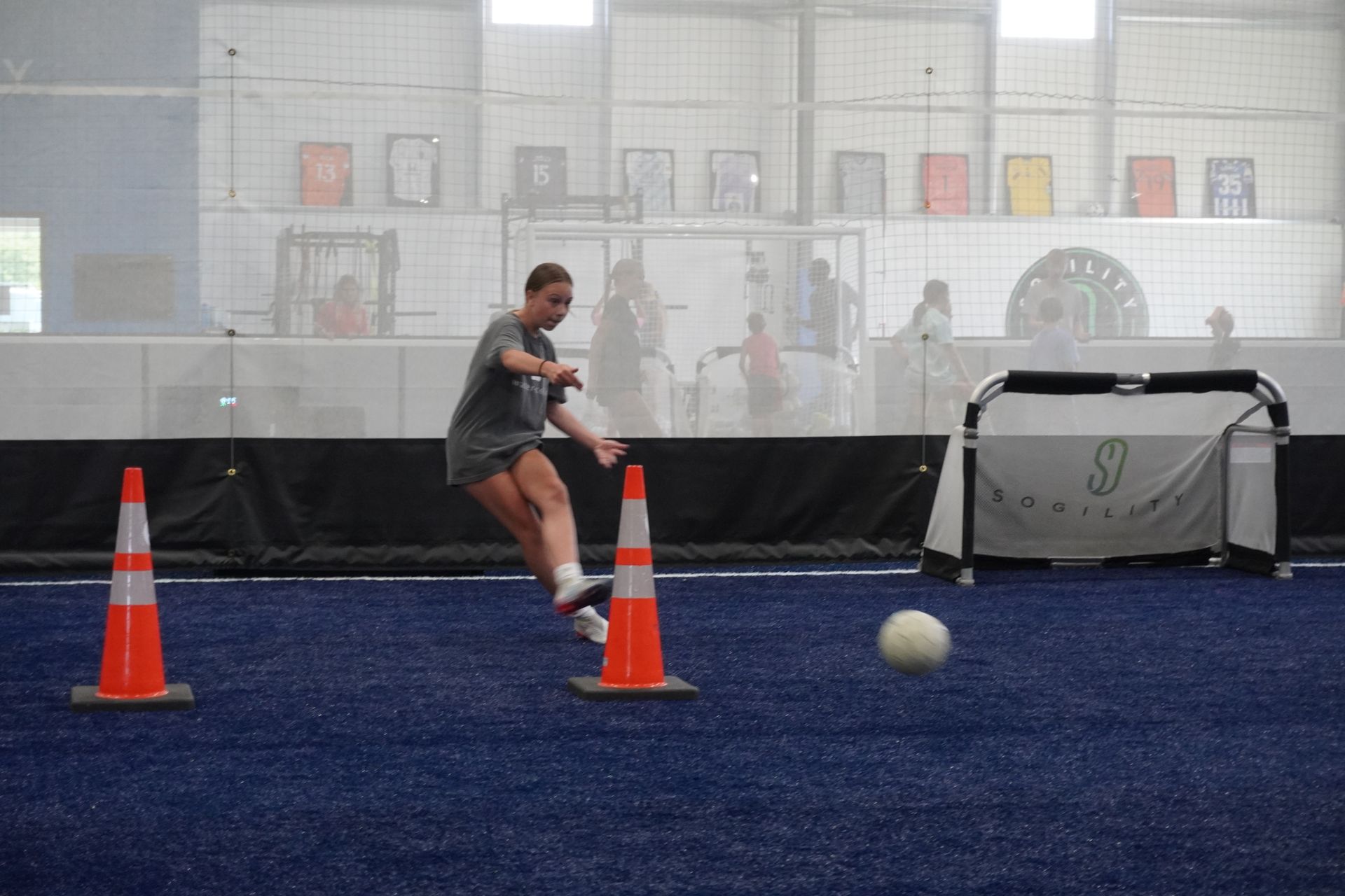 A woman is kicking a soccer ball between two traffic cones.