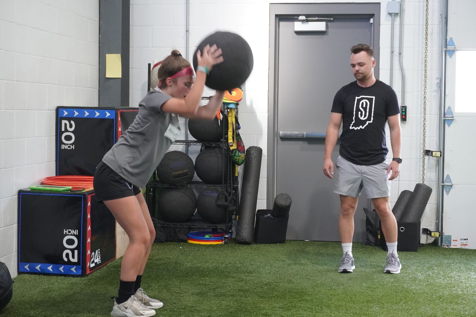 A woman is throwing a medicine ball in a gym while a man watches.