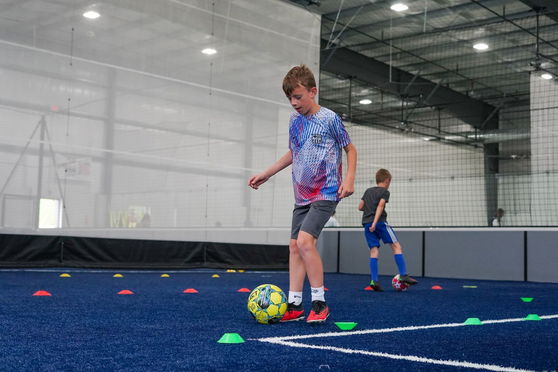 A boy is kicking a soccer ball on an indoor field.