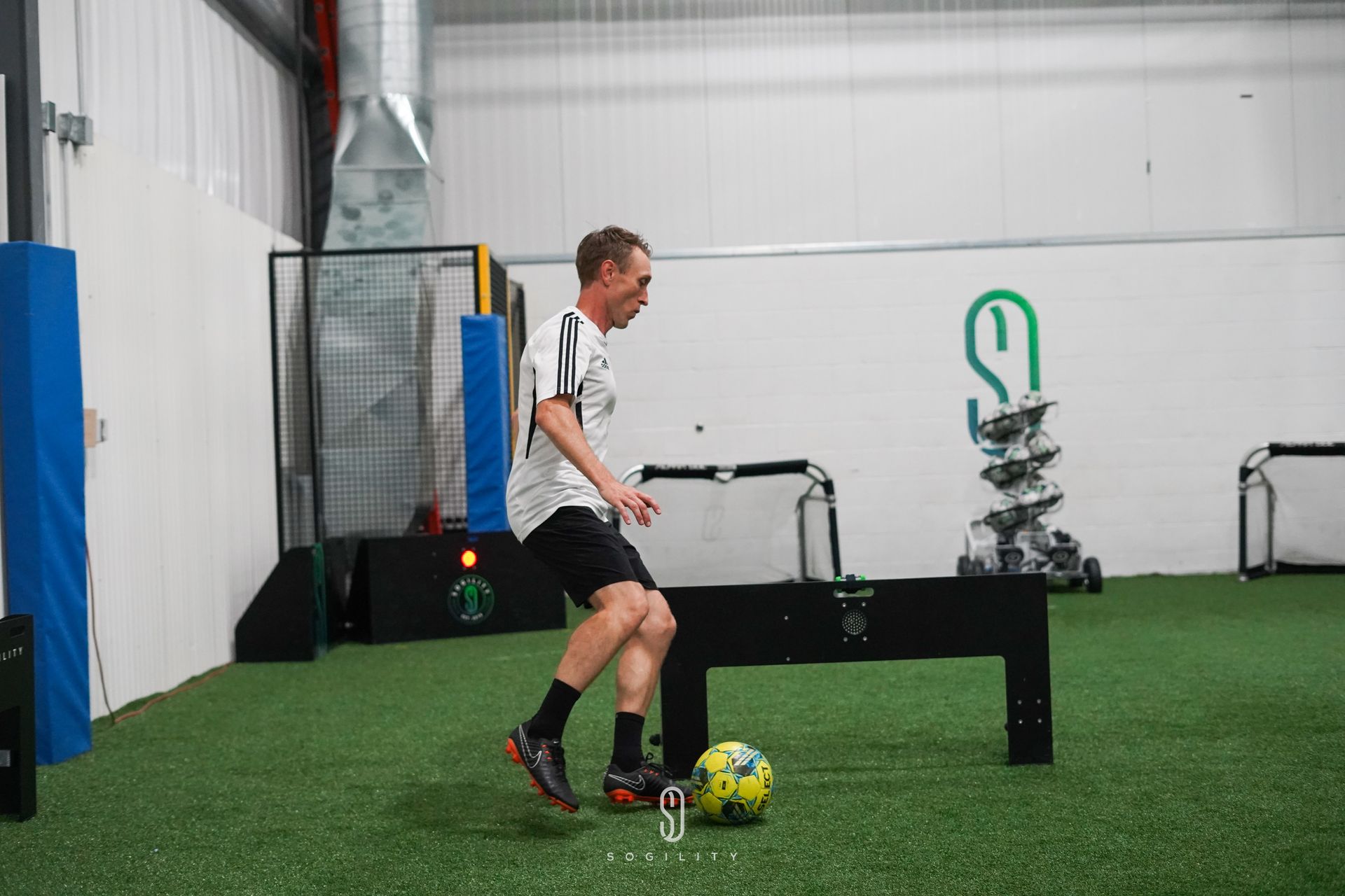 A man is kicking a soccer ball in a gym.