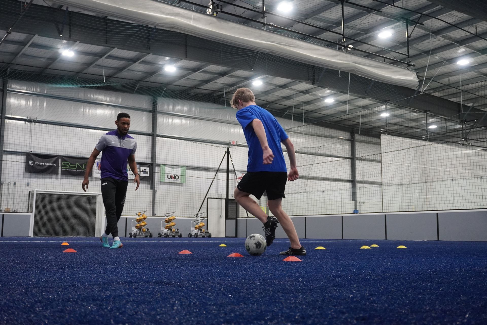 A man and a boy are playing soccer in a gym.