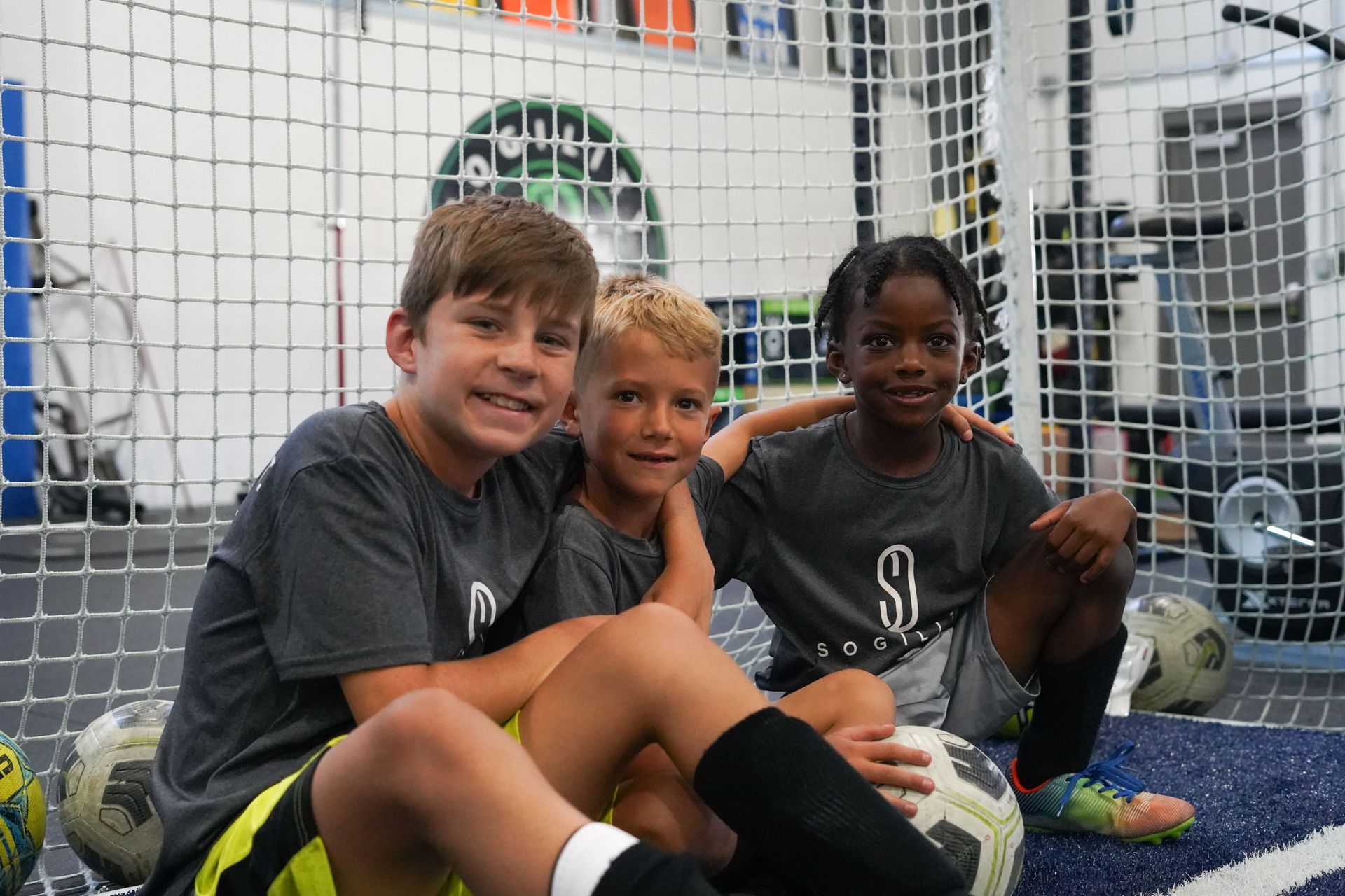 Three young boys are sitting next to each other on a soccer field.