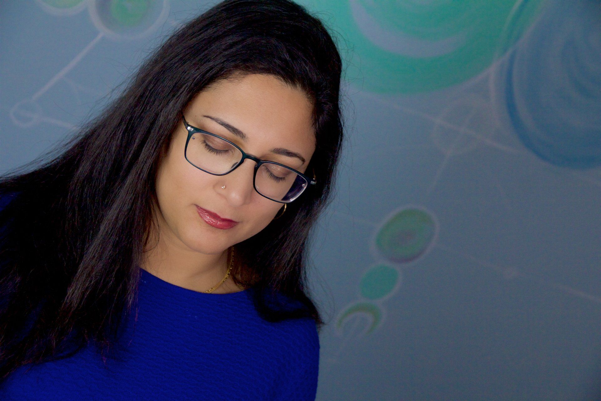 A woman wearing glasses and a blue shirt is looking down.