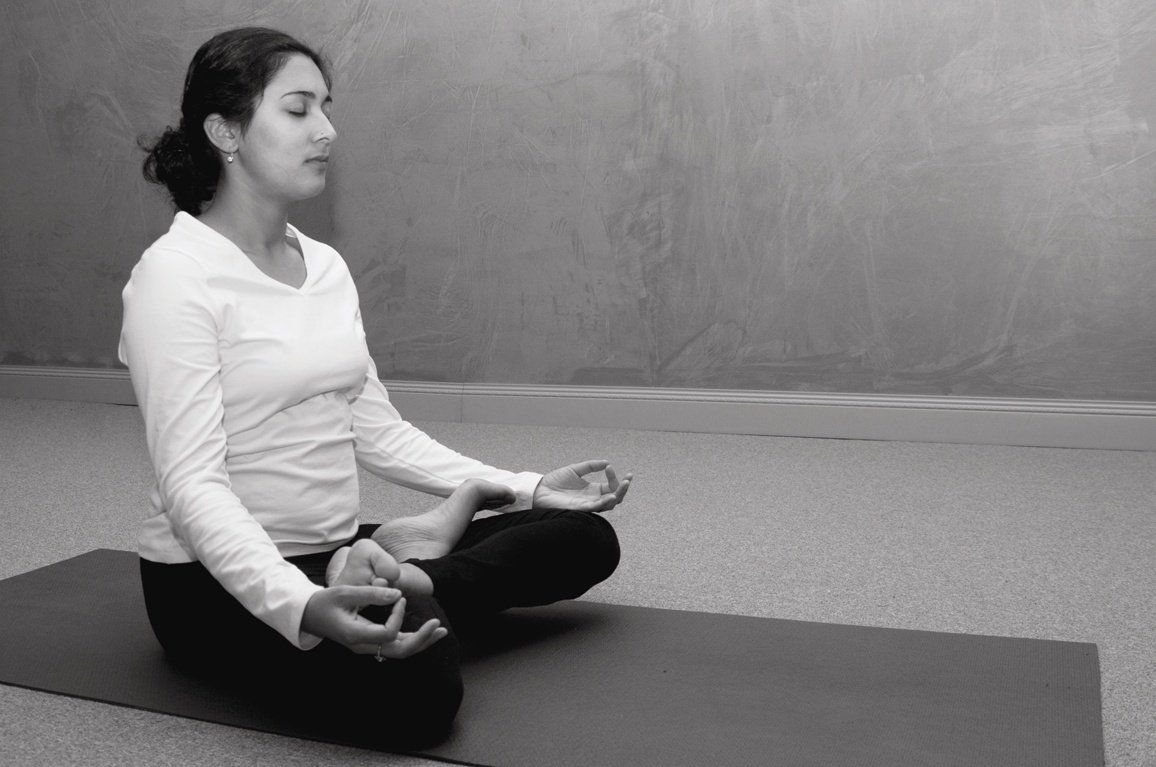 A woman is sitting on a yoga mat with her eyes closed.
