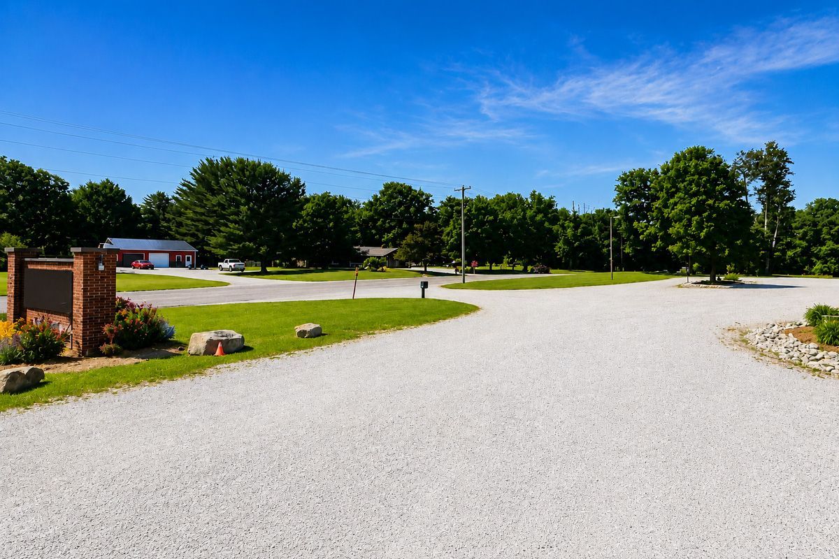 Gravel driveway leading to a small brick building and trees under a bright blue sky.