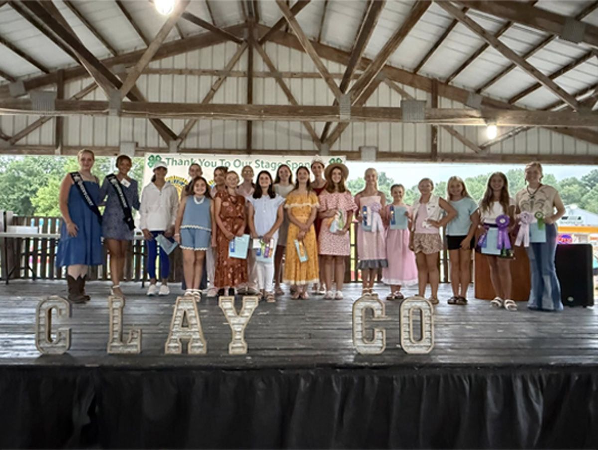 Group of people standing on a stage holding awards under a pavilion, with large “CLAY GO” letters in front.