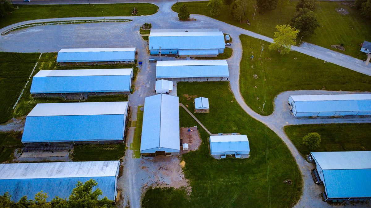 Aerial view of a rural trailer park with rows of white mobile homes and winding roads beside green grass.