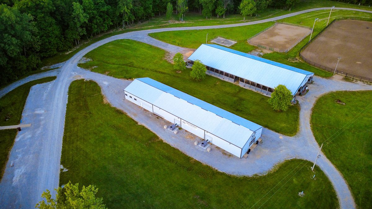 Aerial view of two white farm buildings beside curving gravel roads and green fields.