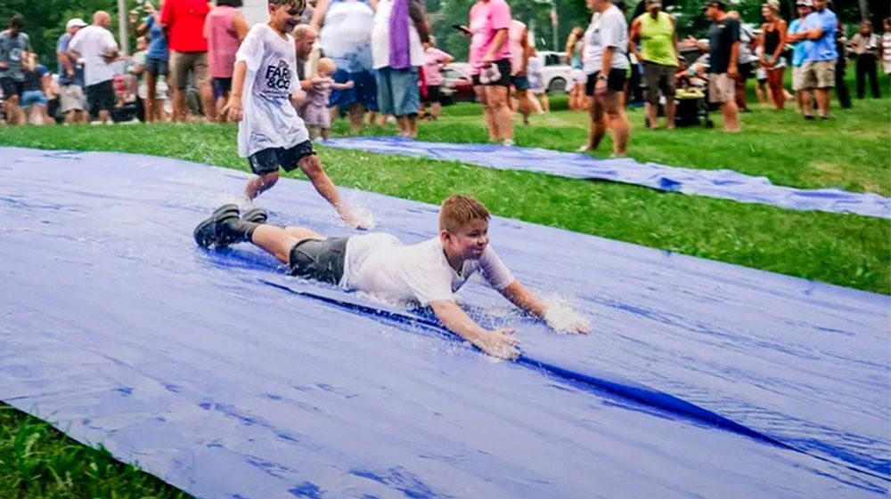 Person sliding face-down on a blue slip-and-slide at an outdoor gathering
