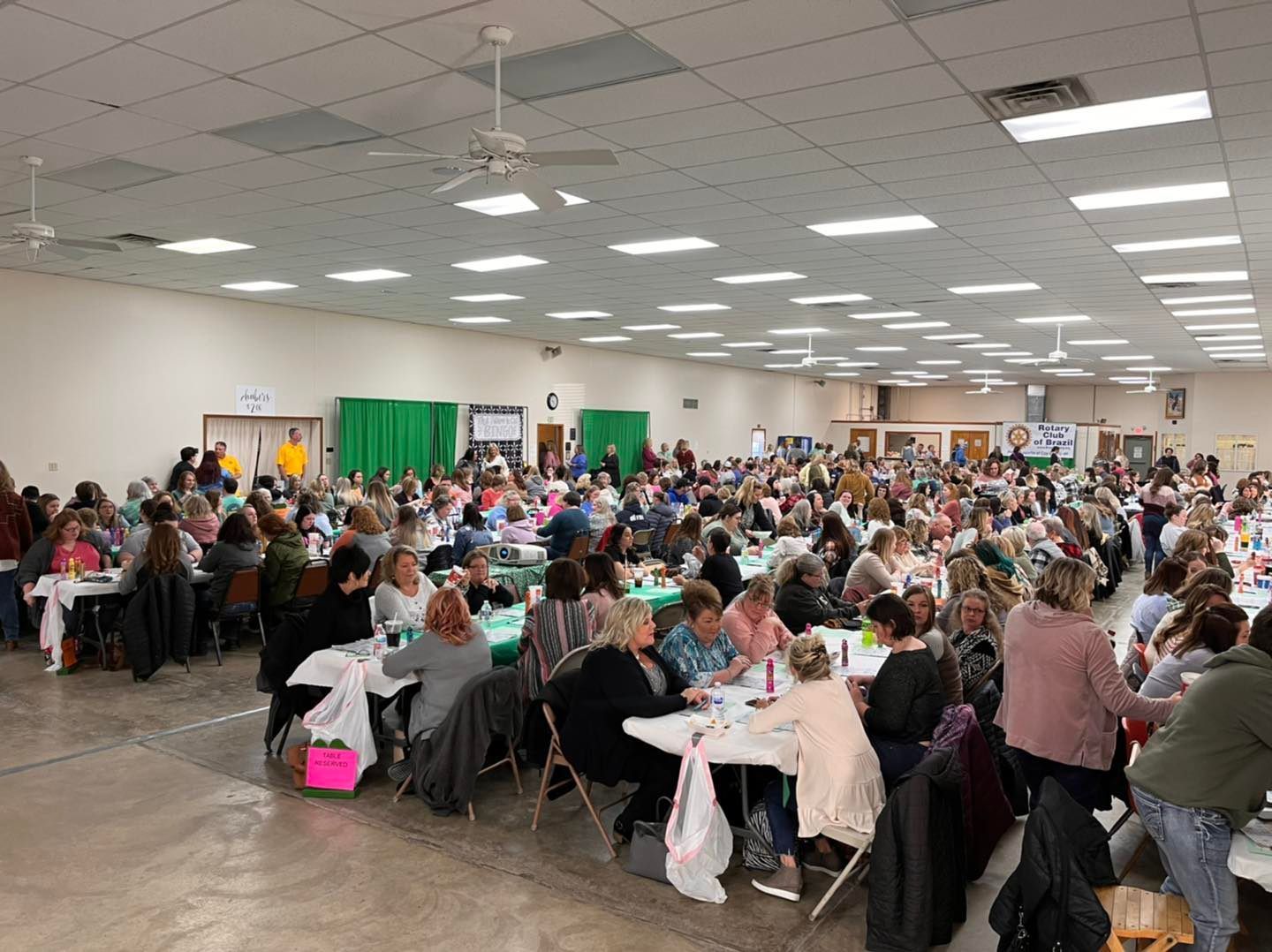 Large banquet hall filled with people seated at round tables for a crowded event or meal