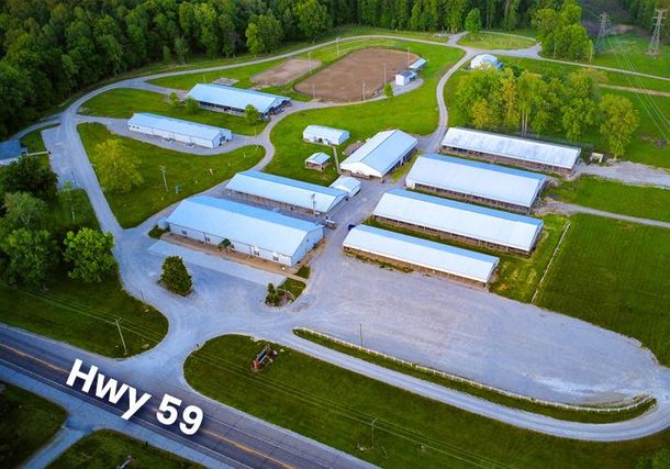 Aerial view of a rural industrial site with white-roofed buildings beside Hwy 59 and trees.