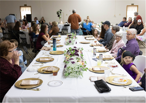 Community meal with people seated at a long banquet table in a bright hall