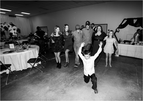 People dancing at a party in a decorated hall, with a child in front raising both arms.