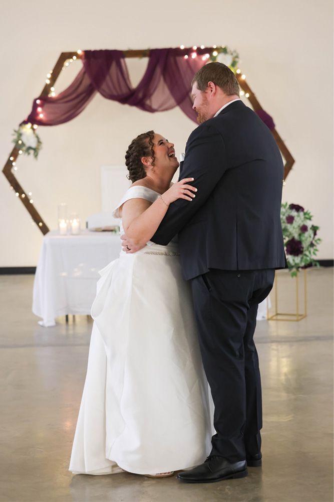 Bride and groom dancing in a decorated indoor wedding venue beneath draped purple fabric