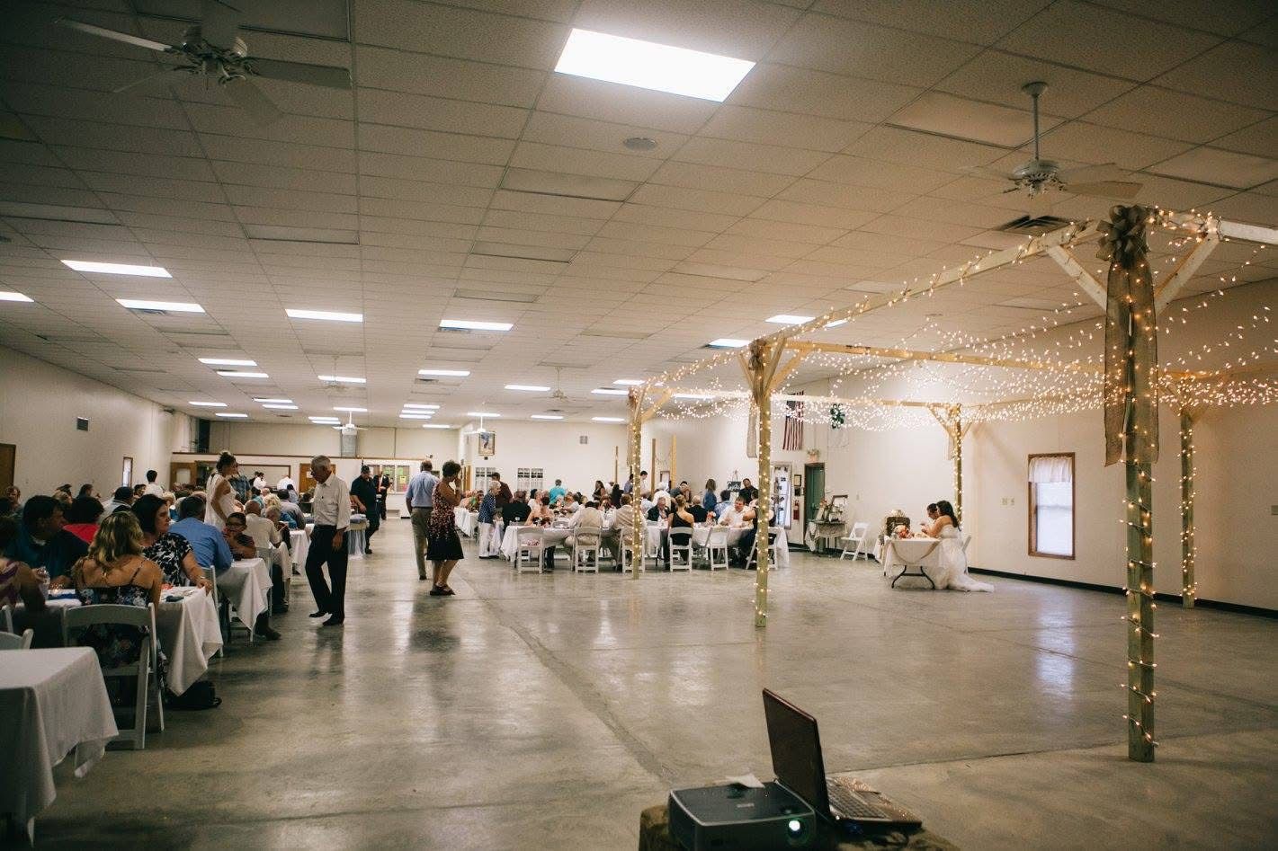 Large indoor banquet hall with guests seated at tables and string lights wrapped around columns.