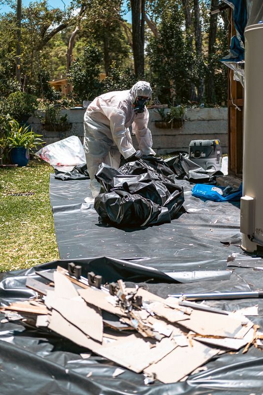 A Man in A Protective Suit Is Kneeling on Top of A Roof — Asbestos Risk Removal In Rockhampton, QLD