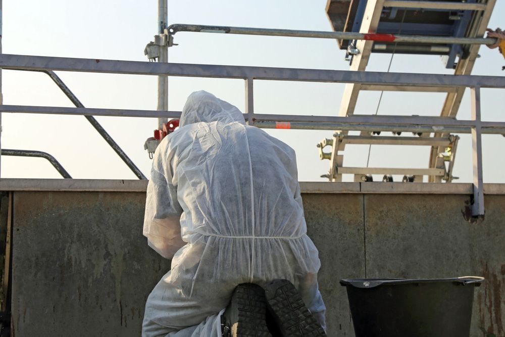 A Man in A Protective Suit Is Kneeling Down — Asbestos Risk Removal In Capricorn Coast, QLD