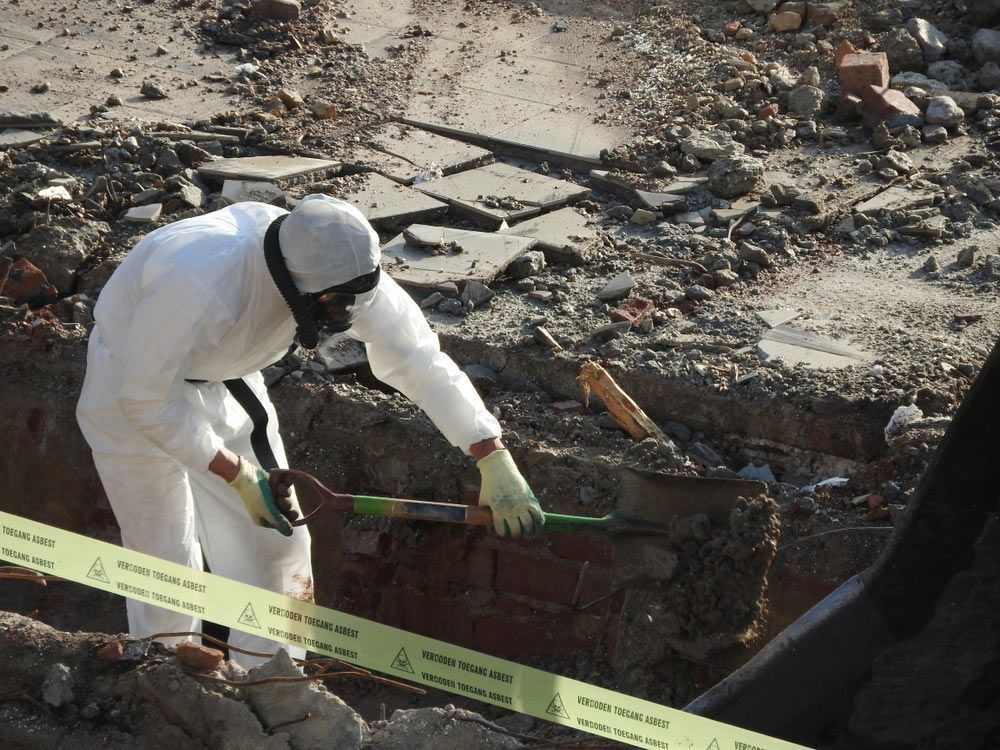 A Man in A Protective Suit Is Digging in The Dirt — Asbestos Risk Removal In Capricorn Coast, QLD