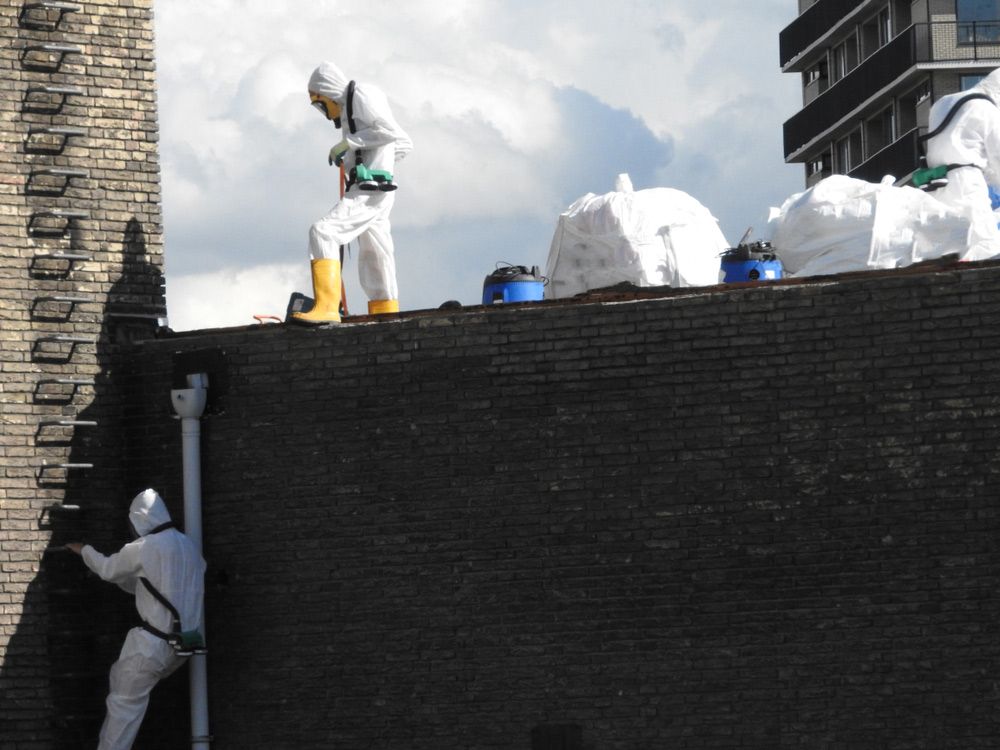A Man in A Protective Suit Is Working on A Brick Wall — Asbestos Risk Removal In Gladstone, QLD