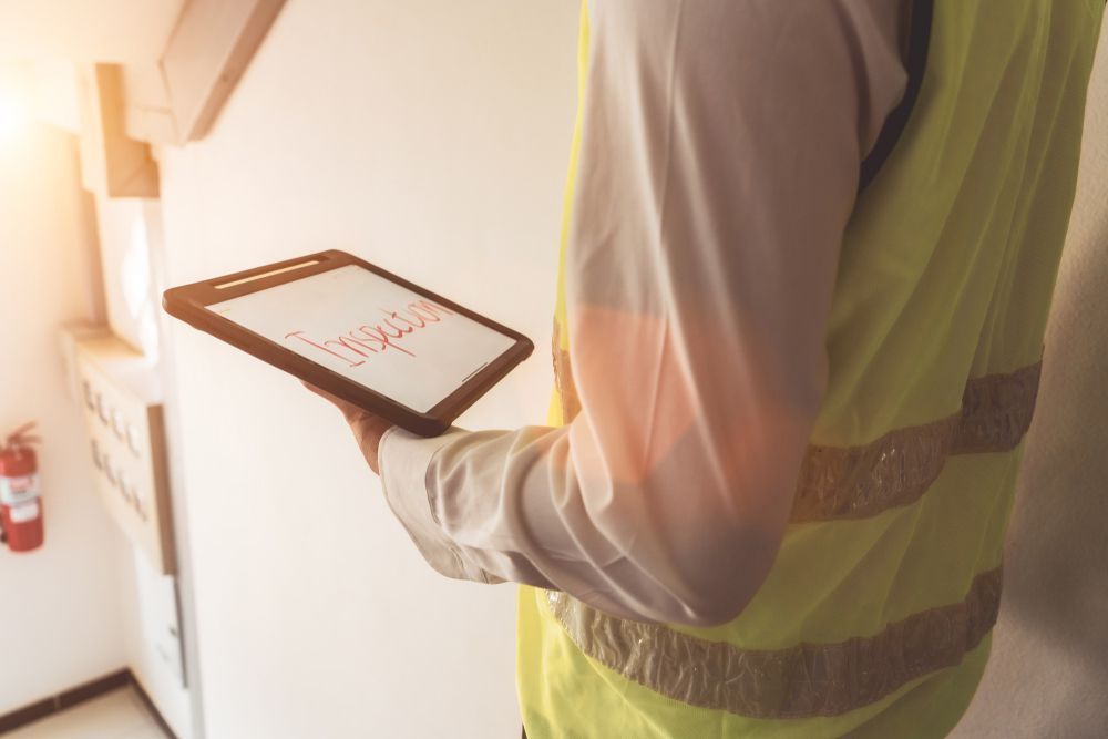 A Man in A Yellow Vest Is Holding a Tablet in His Hand — Asbestos Risk Removal In Rockhampton, QLD