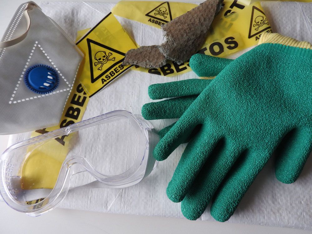 A Pair of Green Gloves Sitting on Top of A White Cloth — Asbestos Risk Removal In Mackay, QLD