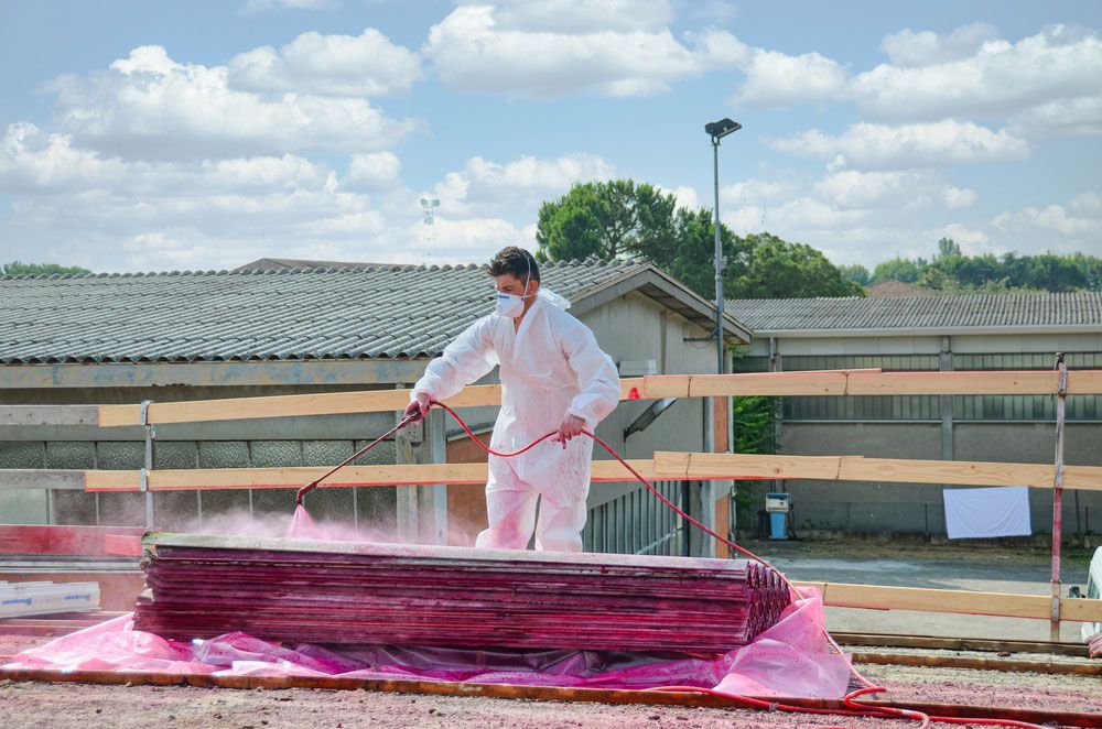 A Man in A White Suit Is Spraying Red Paint on A Stack of Wood — Asbestos Risk Removal In Mackay, QLD