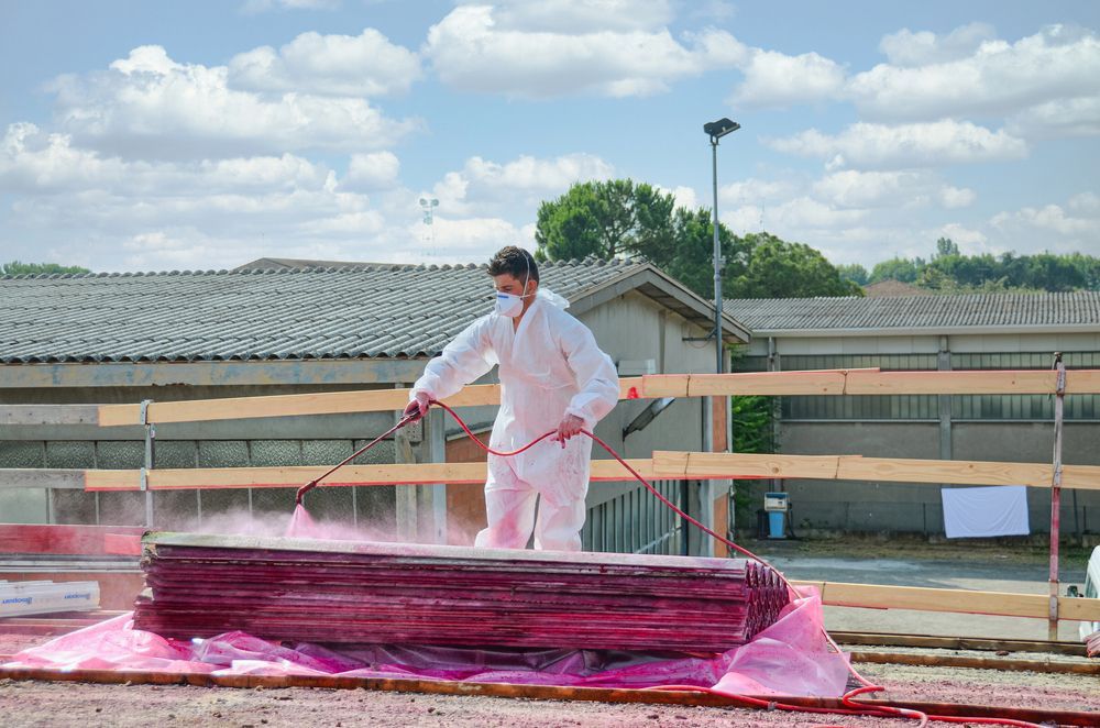 A Man In A White Suit Is Spraying Red Paint On A Piece Of Wood — Asbestos Risk Removal In Gladstone, QLD