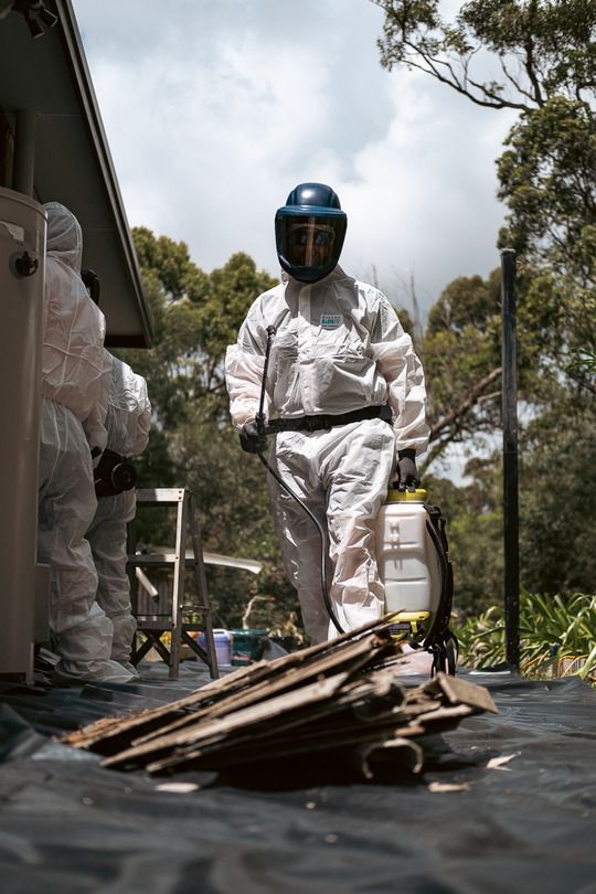 Two Men in Protective Suits Are Kneeling on The Floor — Asbestos Risk Removal In Rockhampton, QLD