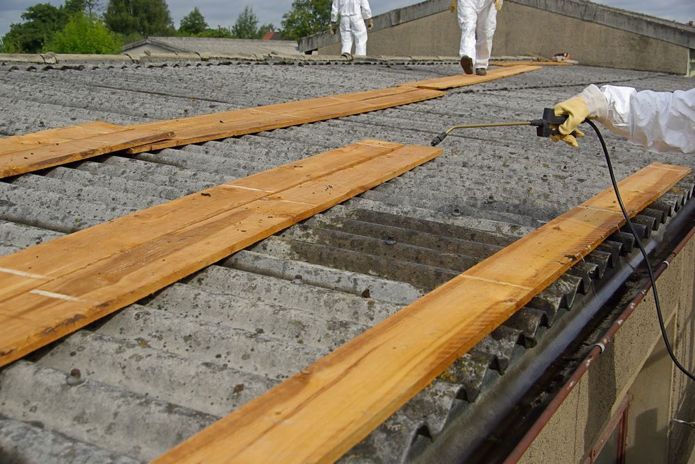 A Person Is Cutting A Piece Of Wood On A Roof — Asbestos Risk Removal In Mackay, QLD