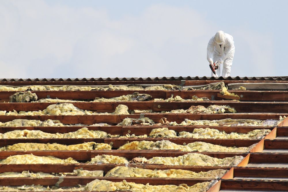 A Man In A White Suit Is Working On The Roof Of A Building — Asbestos Risk Removal In Gladstone, QLD