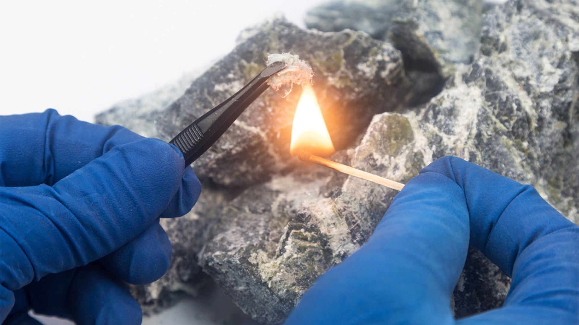 A Person in Blue Gloves Is Lighting a Match on A Rock — Asbestos Risk Removal In Rockhampton, QLD