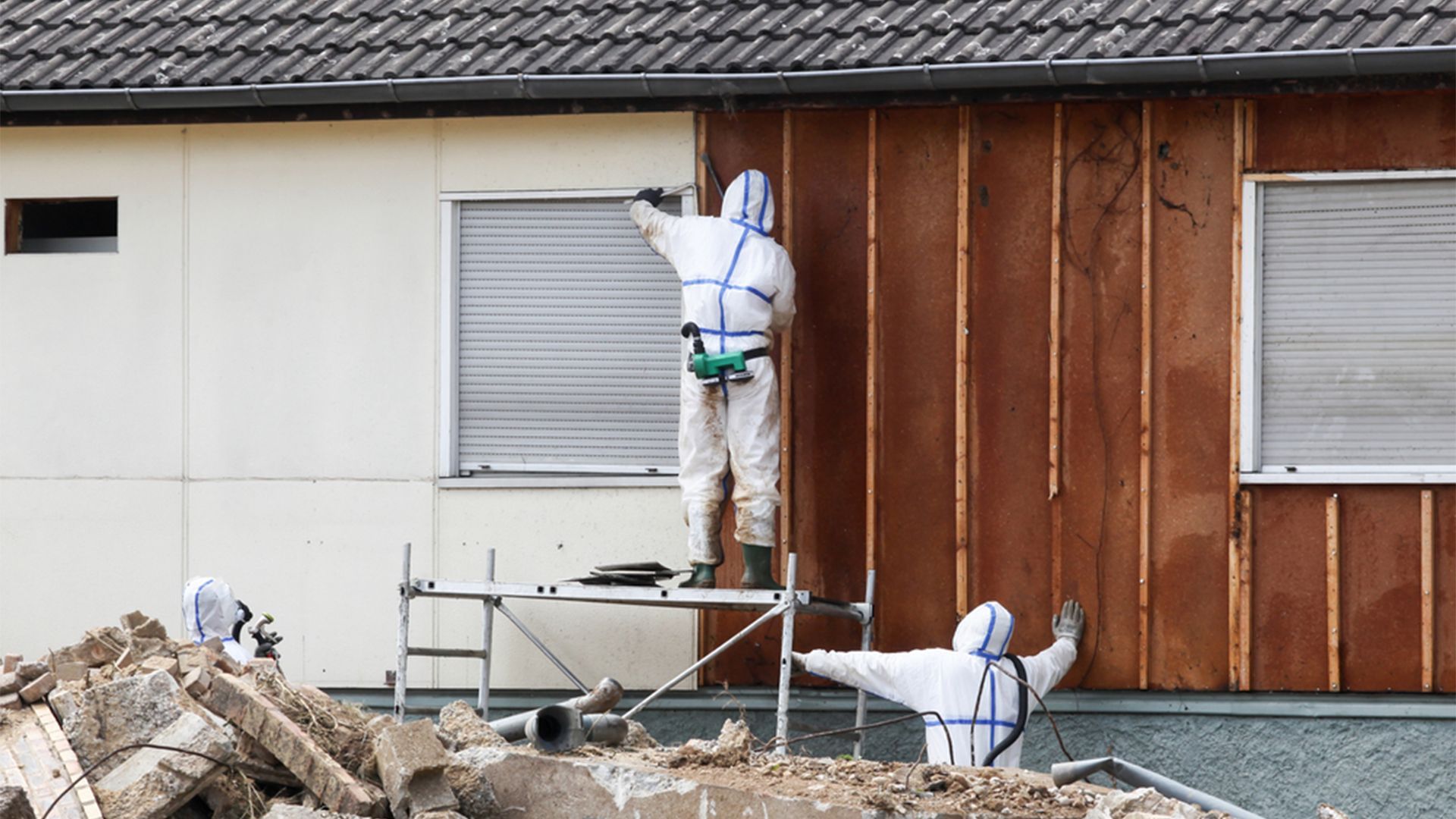 Two Men in Protective Suits Are Working on The Side of A House — Asbestos Risk Removal In Rockhampton, QLD