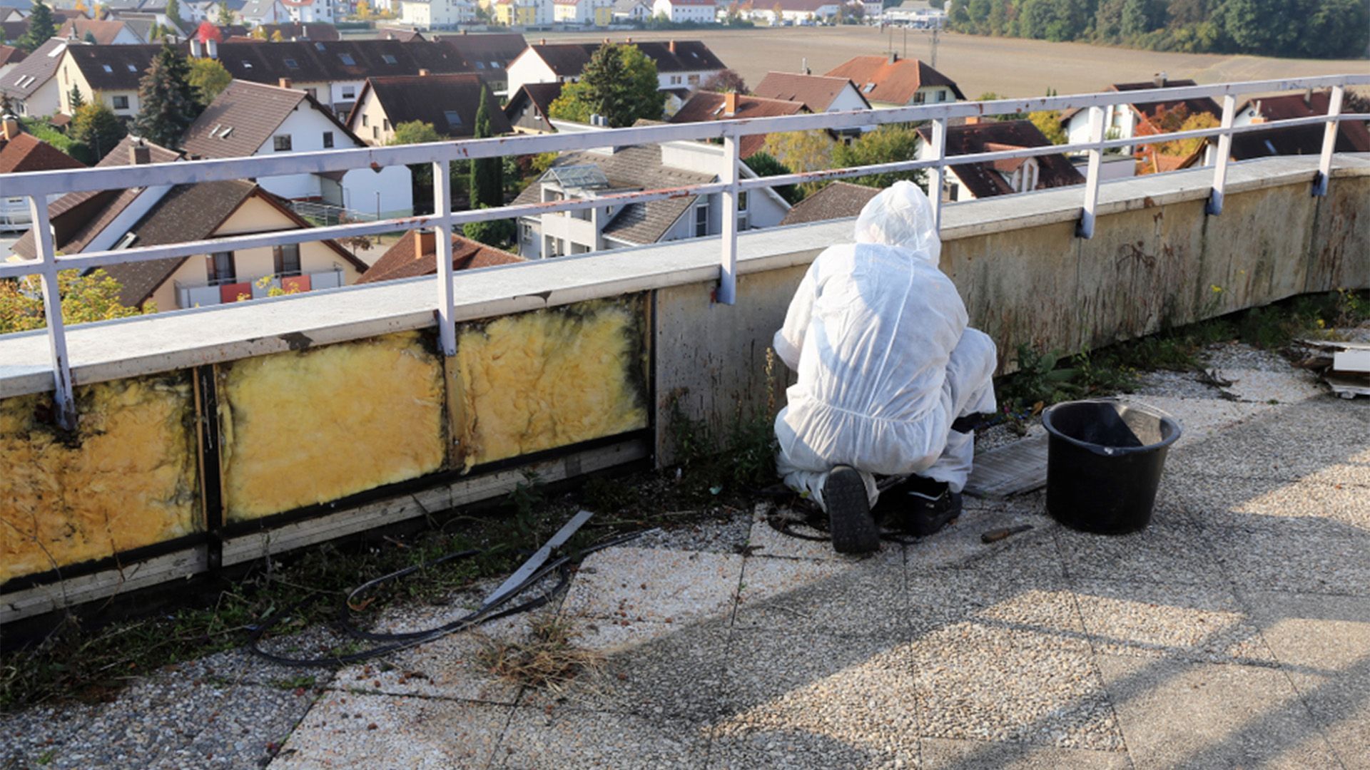 A Man in A Protective Suit Is Working on The Roof of A Building — Asbestos Risk Removal In Rockhampton, QLD