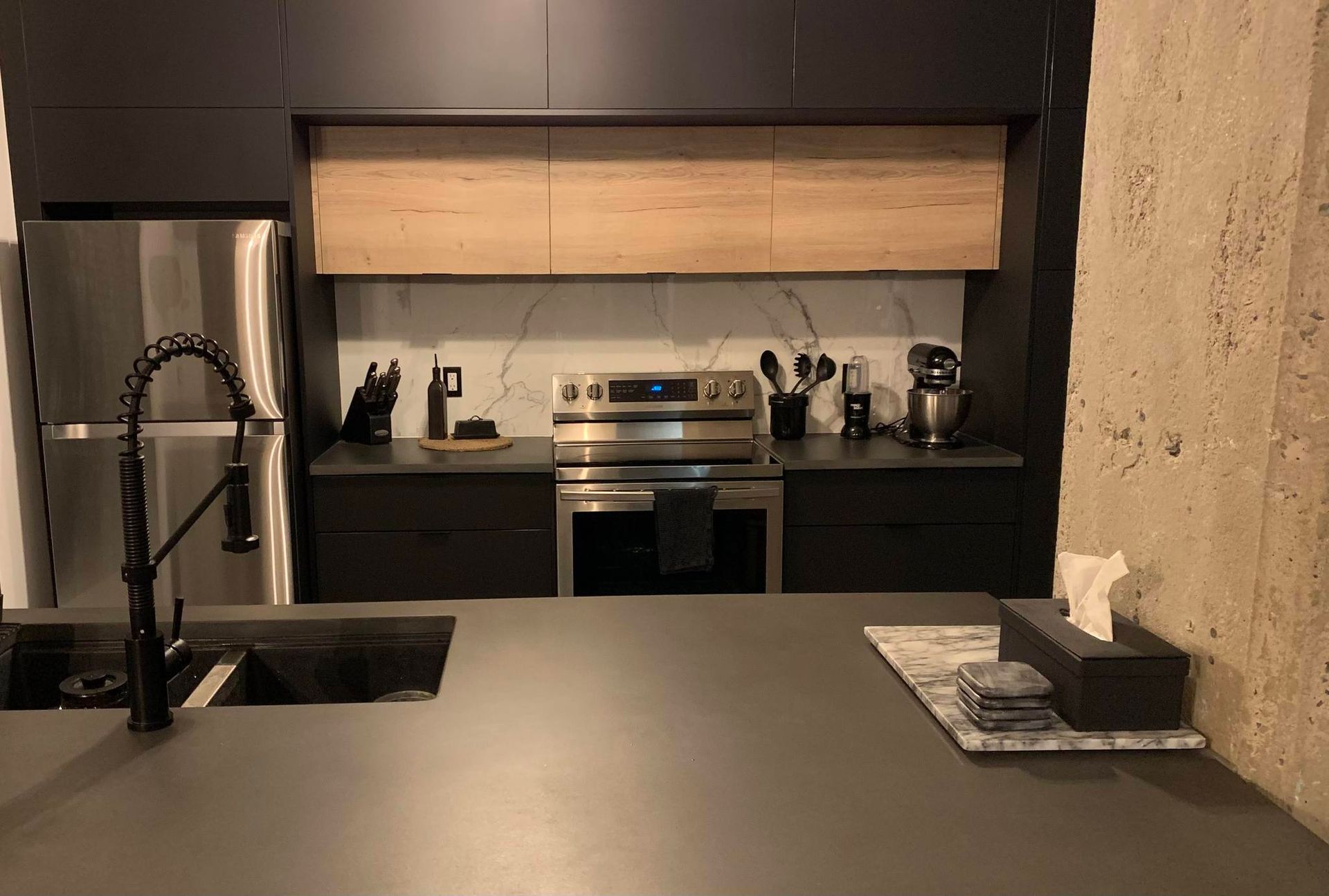 Cuisine moderne avec armoires gris foncé, plafond en bois clair, appareils électroménagers en acier inoxydable et comptoir gris.