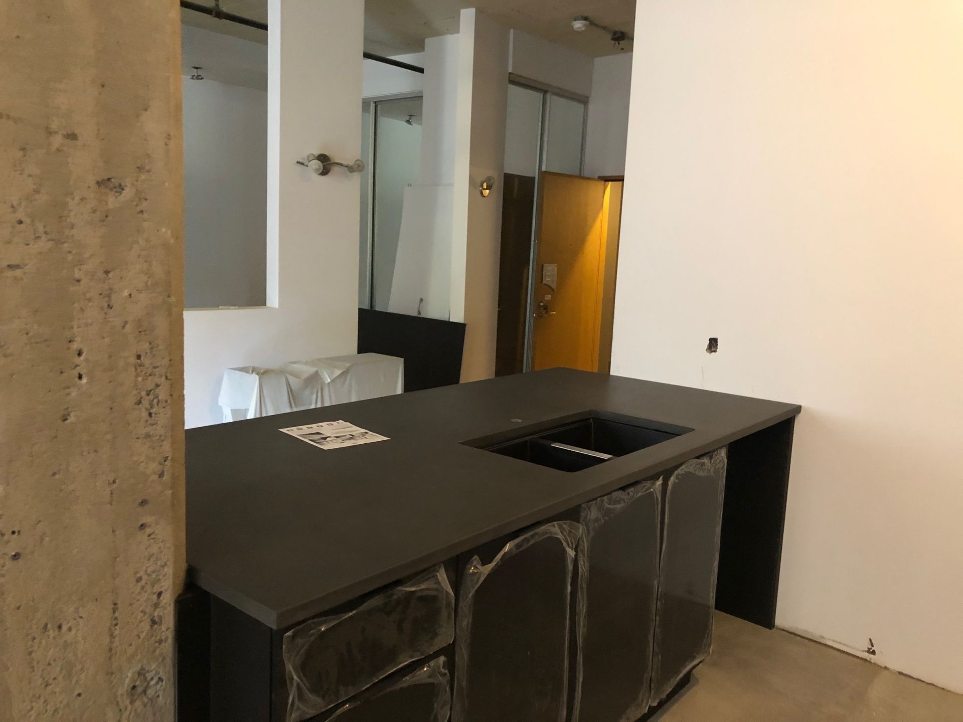 Un îlot de cuisine avec un comptoir noir et un évier se trouve devant une salle de bain.