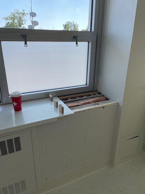 Appui de fenêtre blanc avec des planches de bois partiellement retirées. Une tasse rouge est posée sur le rebord, près d'une fenêtre givrée.