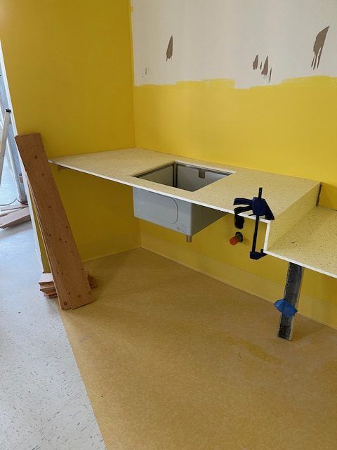 Pièce aux murs jaunes en construction avec un évier. Le plan de travail et les armoires sont en cours d'installation, les pinces étant visibles.