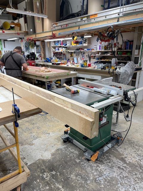 Une personne utilisant une scie circulaire dans un atelier encombré ; des planches de bois sont sur la scie.