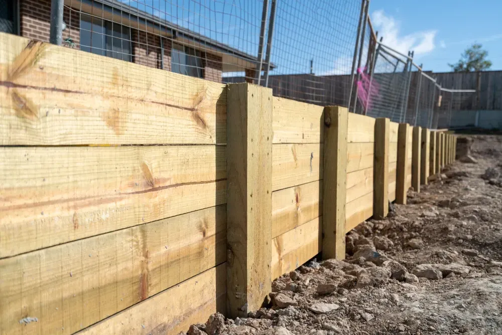 Wooden retaining wall in construction, with posts and horizontal planks, earth ground, blue sky. — Coastline Earthworks in Logan, QLD