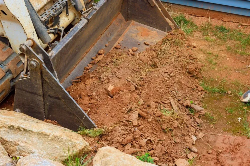 Bobcat bucket filled with dirt, dumping near a building. — Coastline Earthworks in Helensvale, QLD