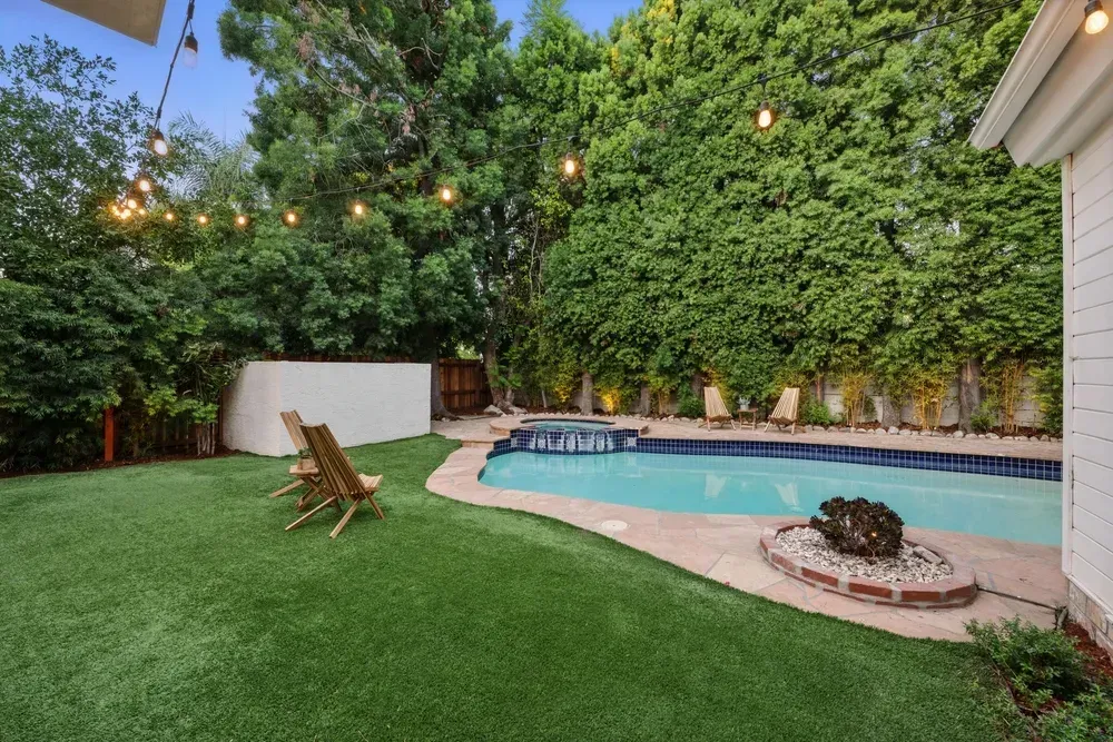 Backyard with pool, artificial grass, wooden chairs, string lights, and lush greenery. — Coastline Earthworks in Logan, QLD