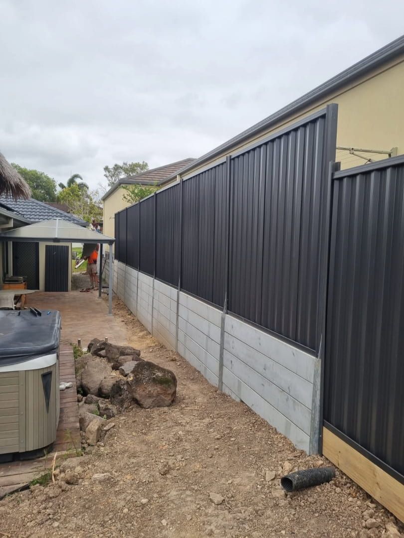 Black corrugated metal fence on a concrete base next to a tan building in a backyard. — Coastline Earthworks in Helensvale, QLD