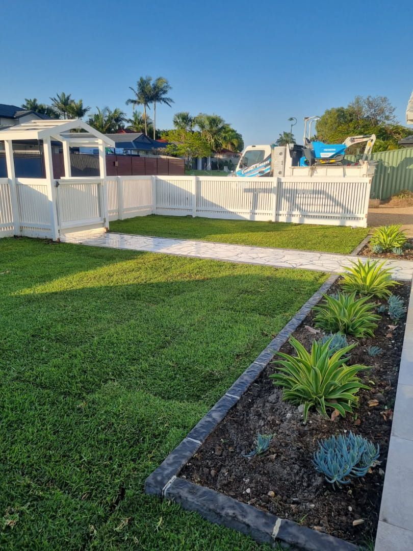 Lawn with white picket fence, a garden bed with plants, and a gazebo on a sunny day. — Coastline Earthworks in Helensvale, QLD